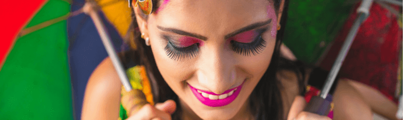 Tendências de maquiagem para o Carnaval 2024 - Mulher maquiada com duas sombrinhas de frevo